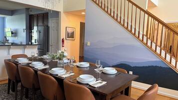 Comedor con mesa dispuesta para seis, cocina al fondo y escalera que sube a un nivel superior.