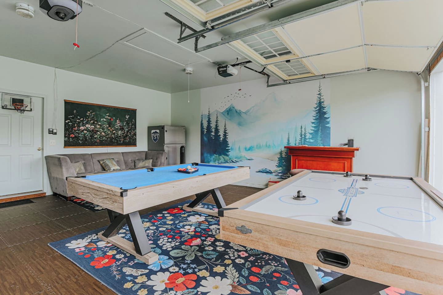 Une pièce comprenant une table de billard, une table de hockey sur air, un canapé, un tableau et une fresque murale.
