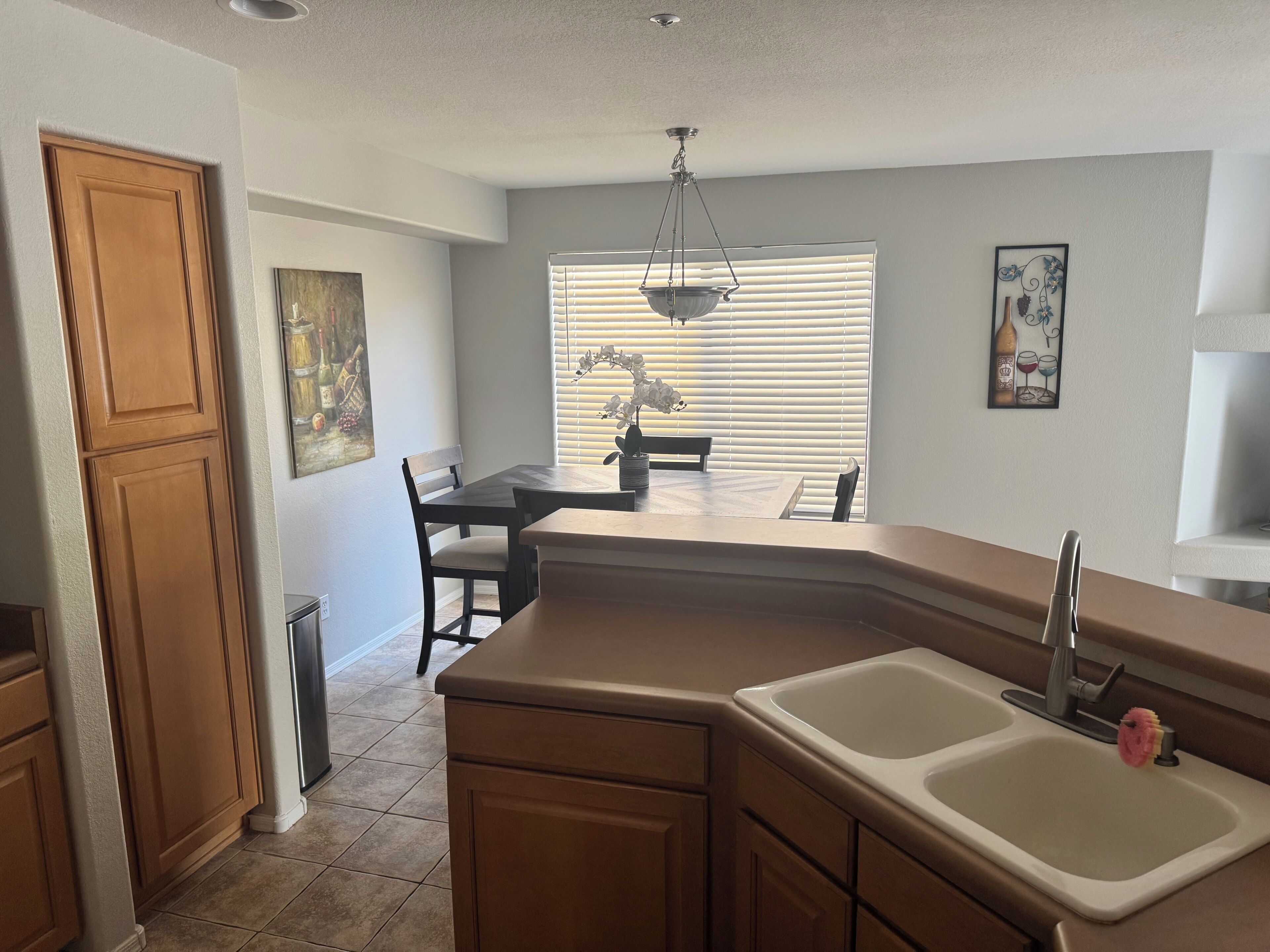 A kitchen with a built-in sink, wooden cabinets, a dining table with chairs, and a hanging light fixture.
