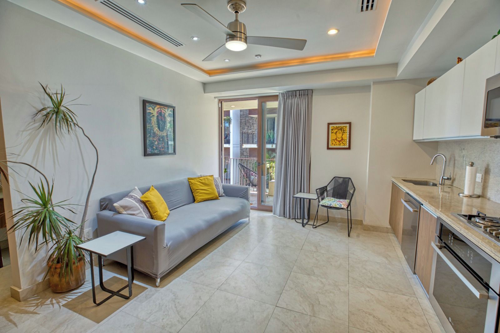A modern living room with a sofa, a small table, a chair, and a kitchen area with a sink and stove.