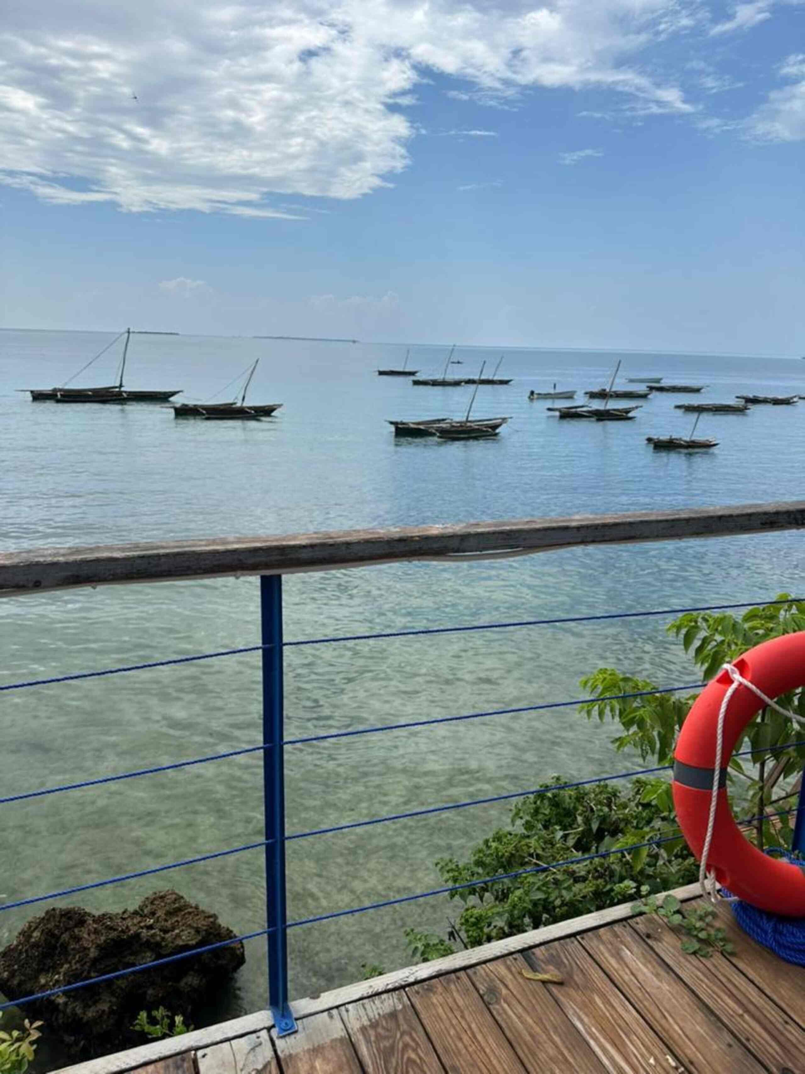 A wooden deck with a railing overlooking calm water with several small boats.
