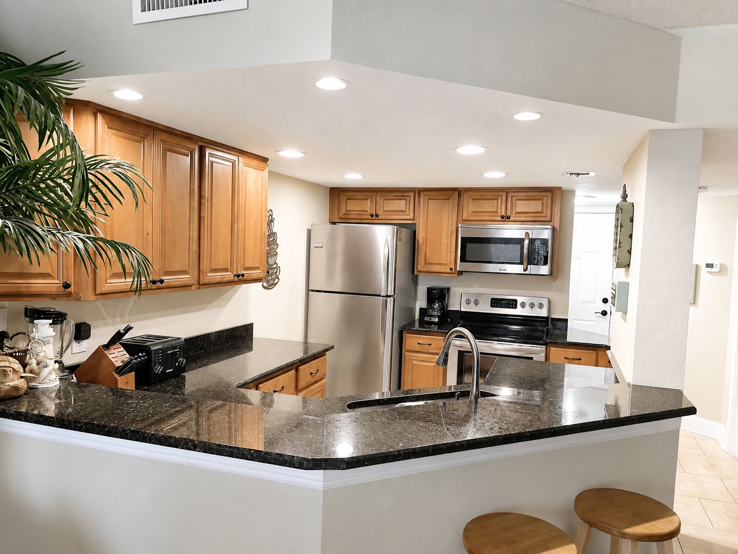 A modern kitchen with wooden cabinets, stainless steel appliances, a granite countertop, and a central island with stools.