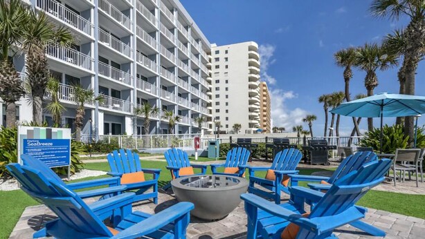 A hotel with a poolside area featuring blue Adirondack chairs and a fire pit.