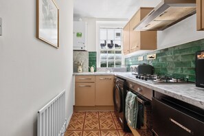 A compact kitchen with a gas stove, a washing machine, and a radiator. - Cozy Apartment Near Hyde Park  (London)