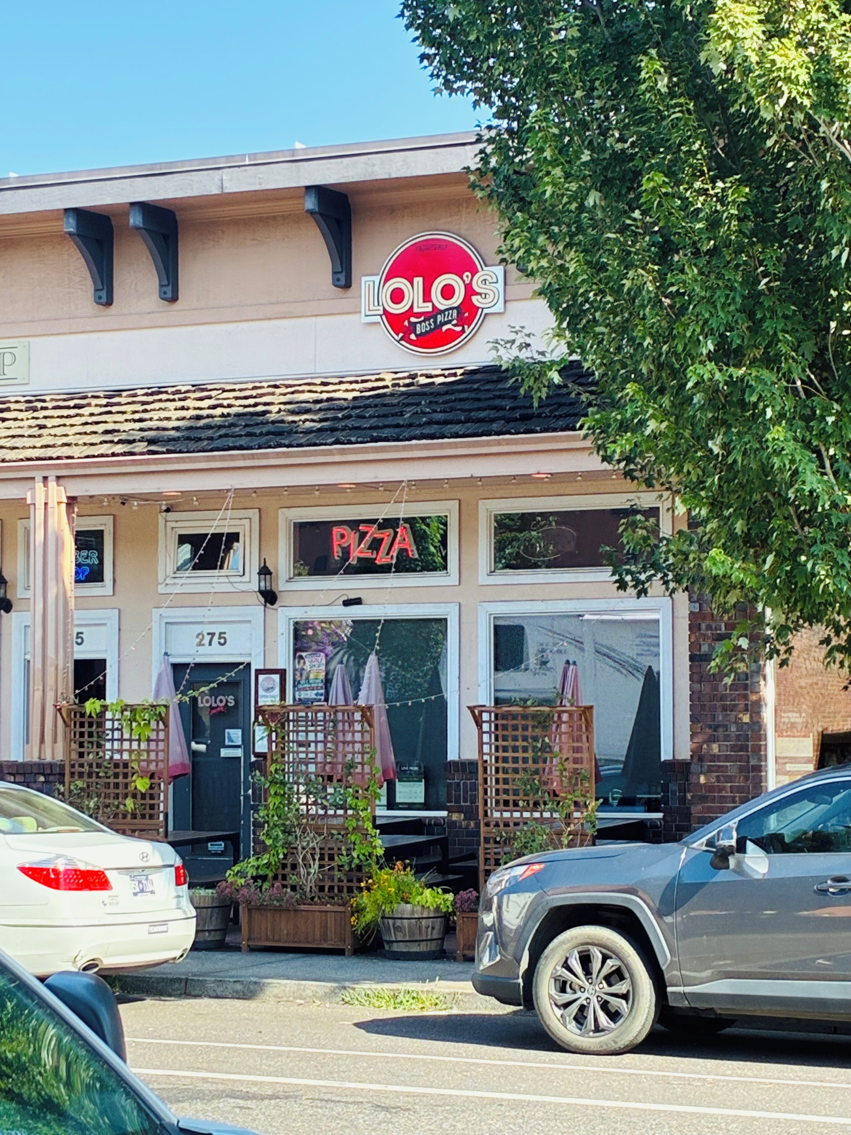 A building with a sign reading 'LOLO'S' and 'PIZZA' indicating a restaurant. There are cars parked in front, and the building has a brick facade with a window displaying a menu.