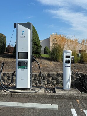 Two electric vehicle charging stations, one larger and one smaller, with a clear sky and a building in the background.