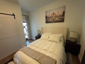 A hotel room with a large bed, a nightstand with a lamp, a window with curtains, and a wall-mounted picture of a famous monument. - Historic 3BR Near Alamodome & River Walk Sleeps 8 (San Antonio)