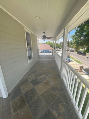 A covered porch with a ceiling fan, a stone-tiled floor, and a view of a street with cars and a house in the background. - Historic 3BR Near Alamodome & River Walk Sleeps 8 (San Antonio)
