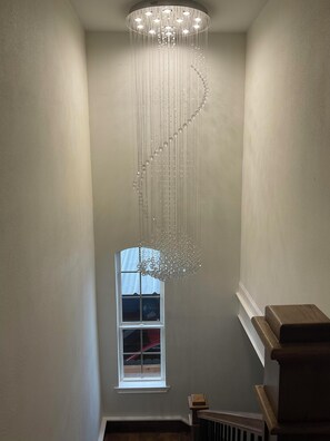 A modern interior with a spiral chandelier, a window, and a wooden staircase. - Historic 3BR Near Alamodome & River Walk Sleeps 8 (San Antonio)