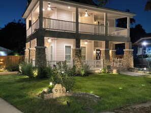 A two-story house with a balcony, stone pillars, and a well-lit front yard. - Historic 3BR Near Alamodome & River Walk Sleeps 8 (San Antonio)