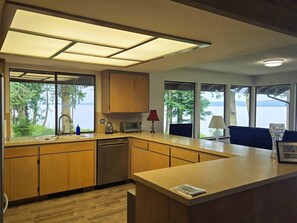 A modern kitchen with a view of the lake, wooden cabinets, a sink, and a countertop with a clock. - Tranquil Bluff retreat W/ Water Views & Game Room (Marrowstone)