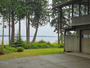A building with a covered porch, a concrete driveway, and a view of a body of water with trees in the background. - Tranquil Bluff retreat W/ Water Views & Game Room (Marrowstone)