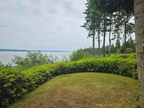 A landscaped area with a view of a body of water, surrounded by trees and a hedge. - Tranquil Bluff retreat W/ Water Views & Game Room (Marrowstone)