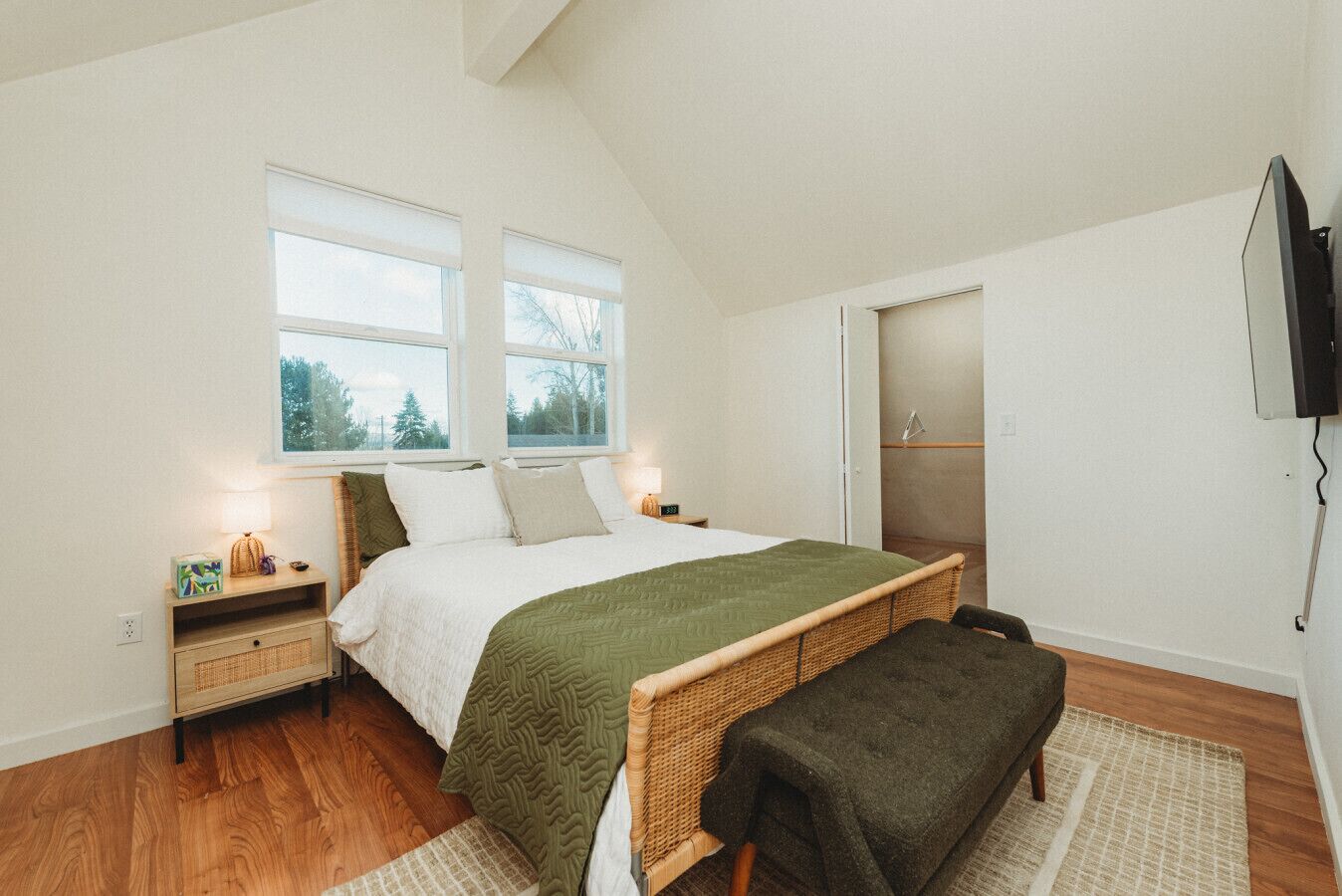 A bedroom with a bed, bedside tables, a bench, a television, and a window.