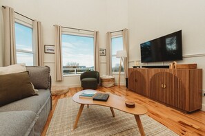A living room with a sofa, armchair, coffee table, and a TV on a wooden cabinet. - Farm Cottage in Sequim w/ Fenced Orchard (Sequim)