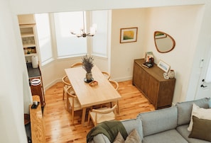 Un comedor con mesa y sillas de madera, un aparador con libros y objetos decorativos, y un sofá en primer plano.