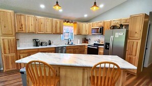 A kitchen with wooden cabinets, a marble countertop, and two wooden chairs. - Cozy Pondside Cabin Near Lake Ouachita (Mount Ida)