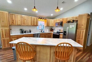 Una cocina con armarios de madera, encimera de mármol y dos sillas de madera.