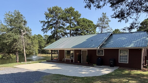 A lodge with a metal roof, a covered porch, and a gravel driveway leading to a lake. - Cozy Pondside Cabin Near Lake Ouachita (Mount Ida)