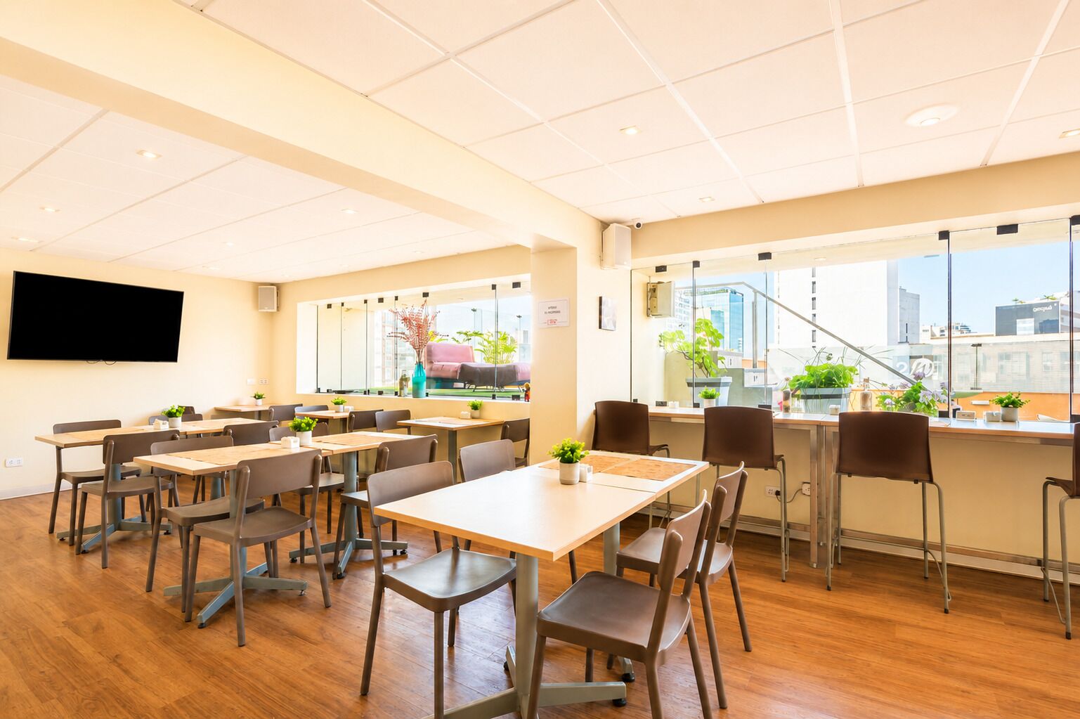 Une salle de conférence équipée de tables et de chaises, d’un téléviseur à écran plat fixé au mur et de grandes fenêtres offrant une vue sur la ville.