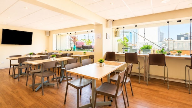 A conference room with tables and chairs, a flat-screen TV on the wall, and large windows with a view of the city. - Diez Canseco 2W Apartments Service (Miraflores)