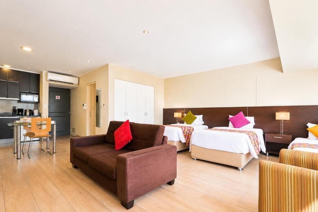 Habitación de hotel con sofá, dos camas, zona de comedor y kitchenette.