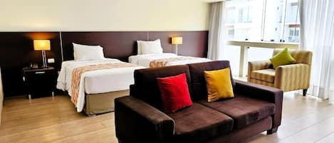 A hotel room with two beds, a sofa, and a chair.