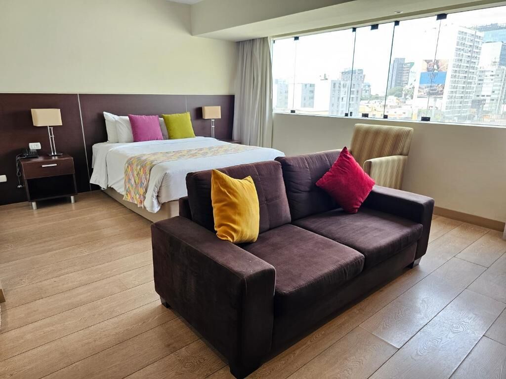 Une chambre d’hôtel avec un lit, un canapé, une table de chevet et une fenêtre donnant sur la ville.