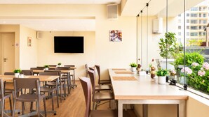 A conference room with tables, chairs, a flat-screen TV, and a window with plants. - Diez Canseco 2W Apartments Service (Miraflores)