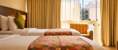A hotel room with two beds, a sofa, and a view of buildings through large windows.