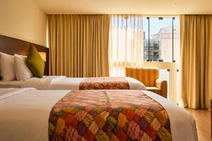 Une chambre d’hôtel avec deux lits, un canapé et une vue sur les bâtiments, grâce à de grandes fenêtres.