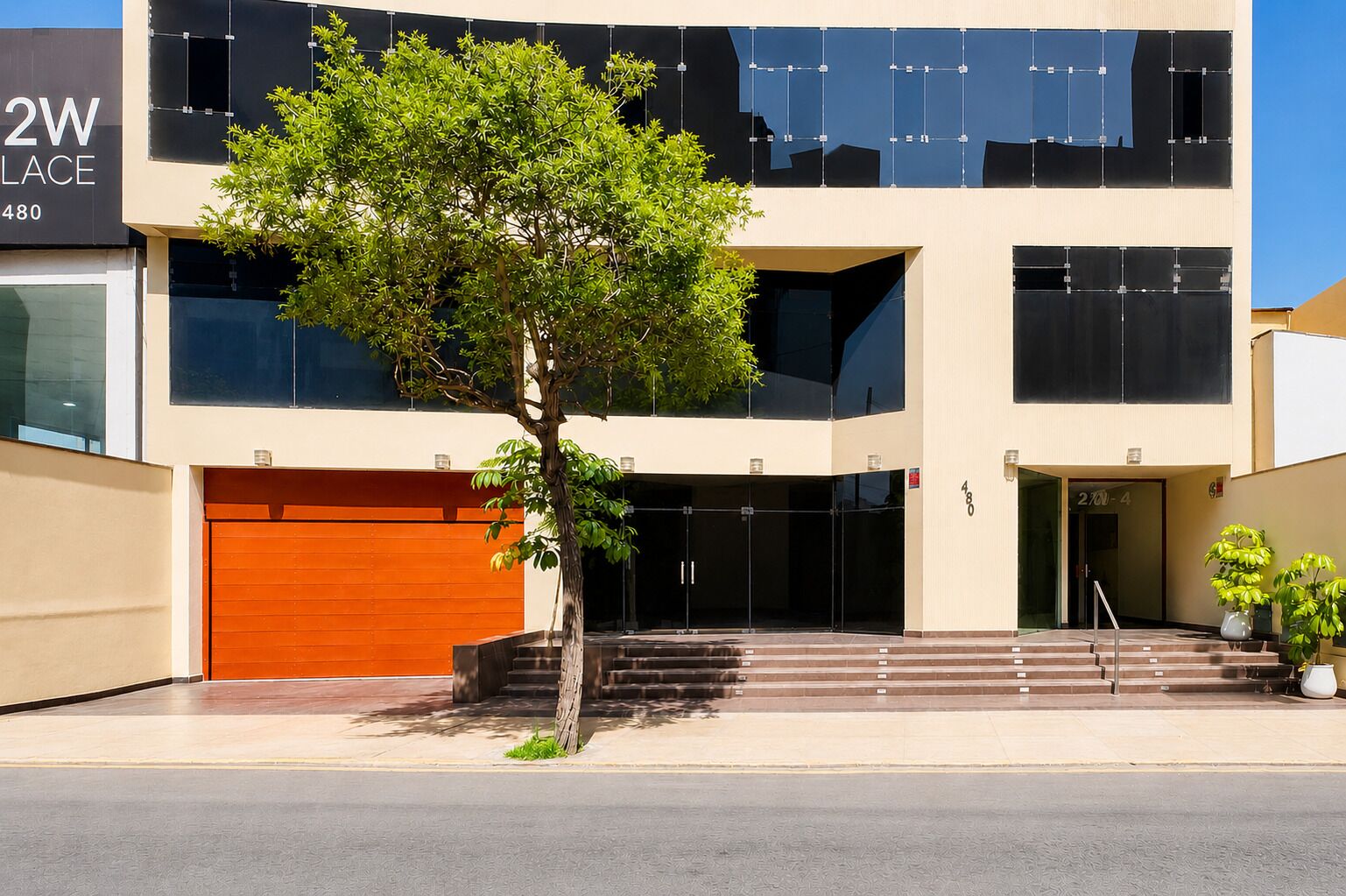 A modern building with a garage, a staircase, and a tree in front.