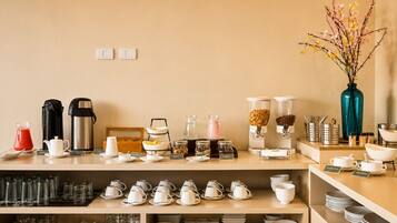 Un buffet de petit-déjeuner d’hôtel proposant une variété de plats et de boissons, notamment des machines à café, un assortiment de fruits et un vase rempli de fleurs.