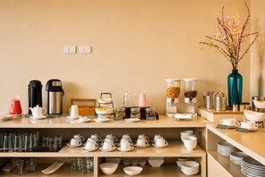 A hotel breakfast buffet with various food and drink options, including coffee makers, a fruit bowl, and a vase with flowers. - Diez Canseco 2W Apartments Service (Miraflores)
