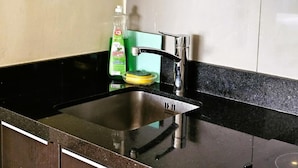 A kitchen with a stainless steel sink, a green bottle of dish soap, and a yellow sponge. - Diez Canseco 2W Apartments Service (Miraflores)