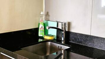Una cocina con un lavamanos de acero inoxidable, una botella verde de lavavajillas y una esponja amarilla.