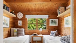 Um quarto de cabana acolhedor, com duas camas, uma janela com vista para o verde e paredes de madeira.