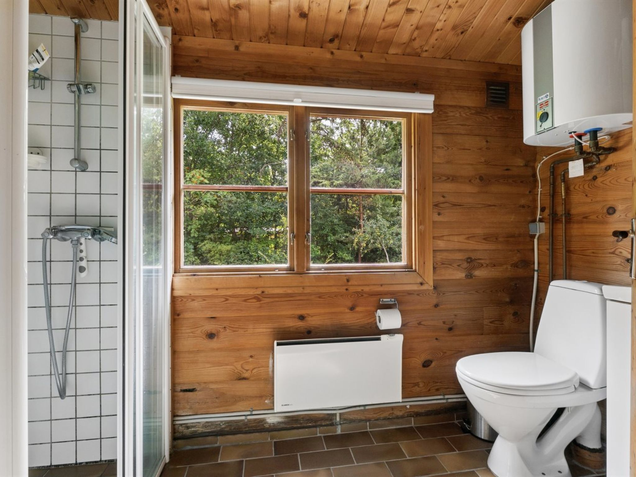 A wooden-paneled bathroom with a window, a toilet, a shower, and a radiator.