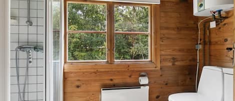 A wooden-paneled bathroom with a window, a toilet, a shower, and a radiator.