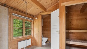 Interior em madeira com janela, vaso sanitário branco e porta que dá acesso a um espaço loft.