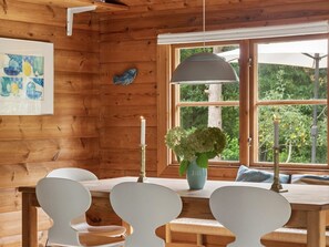 A wooden cabin interior with a dining table, chairs, a hanging light fixture, a window with a view of greenery, and a framed artwork on the wall. - "Greta" - 1.7km from the sea by Interhome (Rørvig)