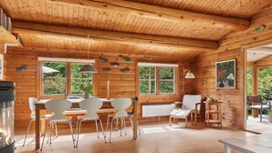 Interior de uma cabana de madeira com área de refeições, cadeiras, mesa e lareira.