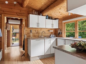 Ein Holzblockhaus-Interieur mit Küchenbereich, Holzbalken an der Decke und einem Fenster mit Blick auf grüne Natur.