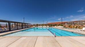A clear blue pool with lounge chairs and a covered area, surrounded by a stone wall and desert landscape. - Desert Oasis - Pool, Hot Tub and Pickleball Courts (Washington)