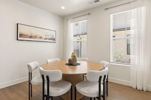 A dining area with a round table, six white chairs, and a framed picture on the wall. - Desert Oasis - Pool, Hot Tub and Pickleball Courts (Washington)