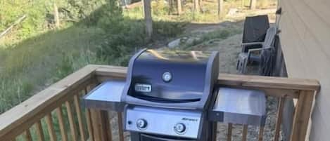 Una parrilla para barbacoa sobre una terraza de madera con barandilla de metal.