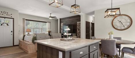 A modern kitchen with a central island, pendant lighting, and a dining area with a round table and chairs.