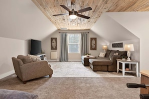 A cozy loft-style living room with a ceiling fan, a flat-screen TV, and a large window with curtains. - Brand New Home @ Lake Granby w/4 Bedrooms & 2 Living Rooms (Grand Lake)