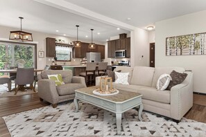 A modern living room with a beige sofa, a coffee table, and a dining area with chairs and a table. - Brand New Home @ Lake Granby w/4 Bedrooms & 2 Living Rooms (Grand Lake)