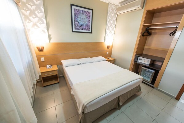 Ein Hotelzimmer mit Bett, Nachttischen, einem Kleiderschrank, einem Wandbild und einer Minibar.